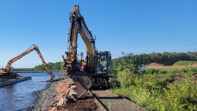 Hi-Rail excavator moves along railway, with water on the left side