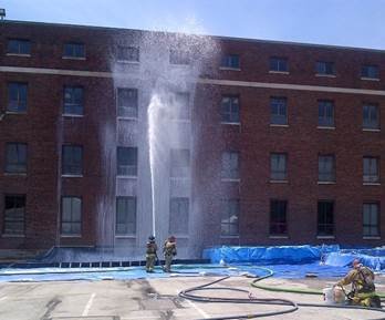 Firefighters spray foam on a brick building.