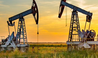 Two pumpjacks for oil extraction in the foreground of an open field, deep yellow sunset in the background.