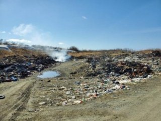 A landfill with smoke coming off of a pile.
