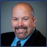 A person with a bald head and short dark goatee, smiling.